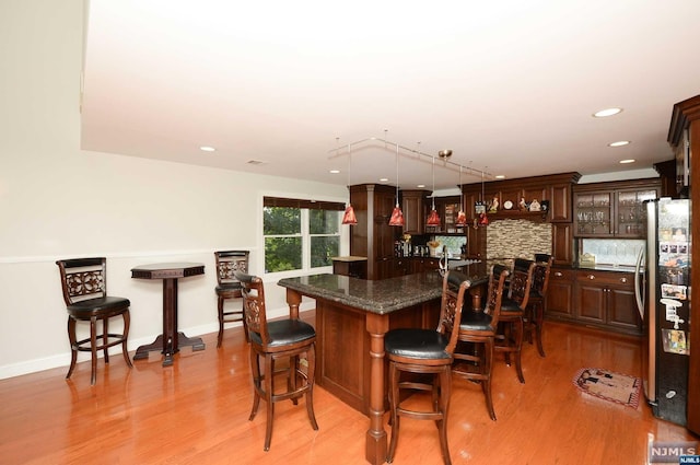 bar featuring stainless steel refrigerator, light hardwood / wood-style flooring, hanging light fixtures, and dark brown cabinets