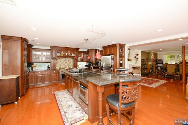 kitchen featuring sink, light wood-type flooring, decorative light fixtures, and an island with sink