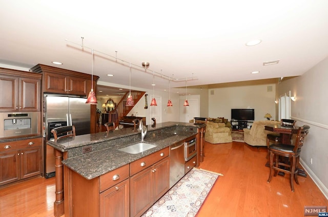 kitchen with decorative light fixtures, light hardwood / wood-style floors, a kitchen island with sink, and dark stone counters