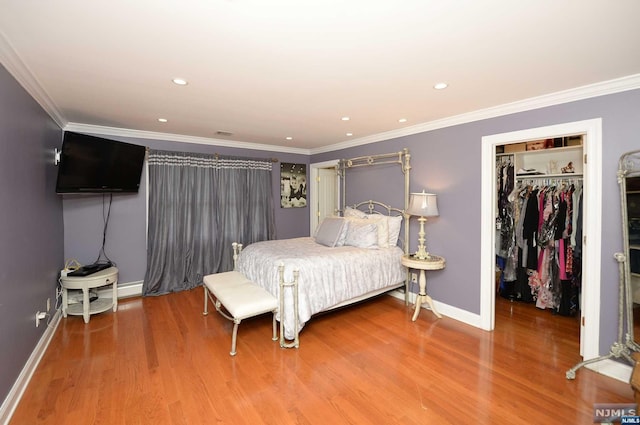 bedroom with hardwood / wood-style flooring, a walk in closet, ornamental molding, and a closet