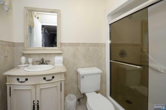 bathroom featuring walk in shower, vanity, toilet, and tile walls