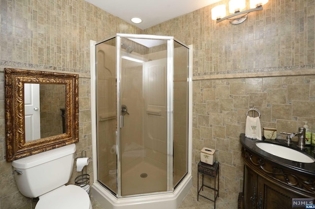 bathroom featuring vanity, a shower with shower door, tile walls, and toilet