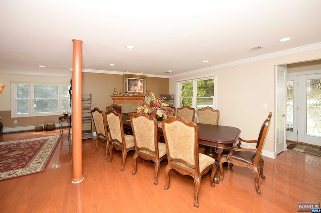 dining space featuring light wood-type flooring, ornate columns, and ornamental molding