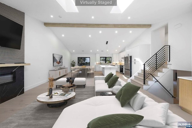 living room featuring a skylight, beamed ceiling, and light hardwood / wood-style floors