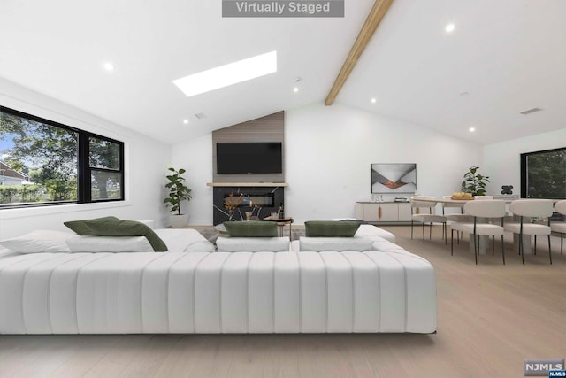 living room featuring vaulted ceiling with skylight and light wood-type flooring