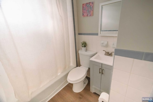 full bathroom with vanity, wood-type flooring, shower / bathtub combination with curtain, tile walls, and toilet