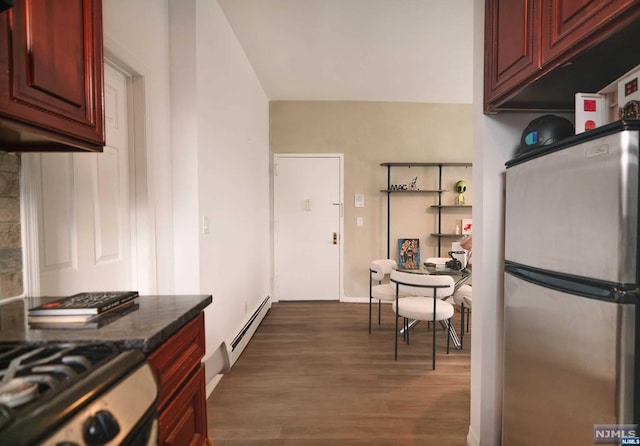 kitchen featuring dark hardwood / wood-style flooring, stainless steel refrigerator, baseboard heating, and dark stone countertops