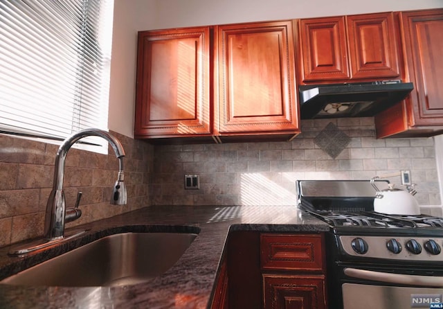 kitchen with gas range, decorative backsplash, sink, and dark stone counters