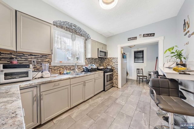 kitchen featuring light stone countertops, sink, stainless steel appliances, backsplash, and gray cabinets