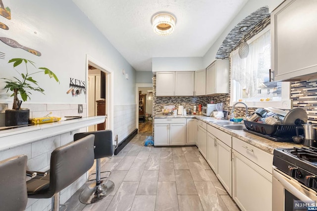 kitchen featuring a textured ceiling, backsplash, gas range gas stove, and sink