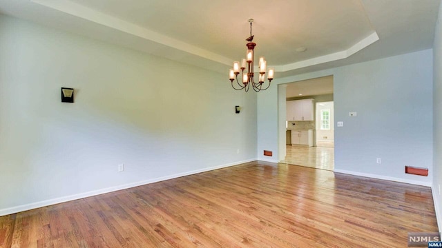 spare room featuring light wood-type flooring, a tray ceiling, and an inviting chandelier