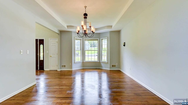 unfurnished dining area with a raised ceiling, dark hardwood / wood-style floors, and an inviting chandelier