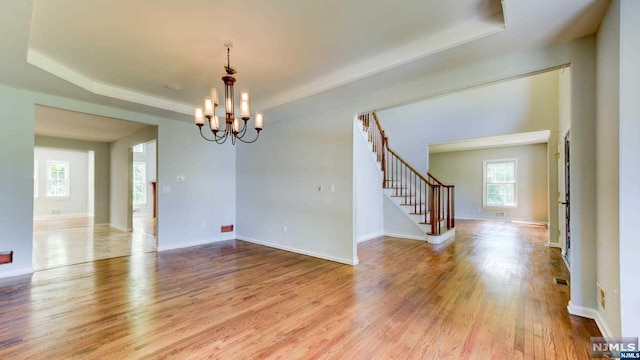 spare room with a notable chandelier, a raised ceiling, and light wood-type flooring