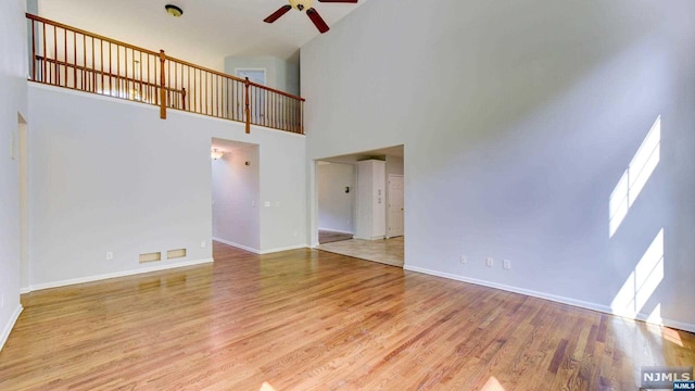 unfurnished living room with light wood-type flooring, a towering ceiling, and ceiling fan