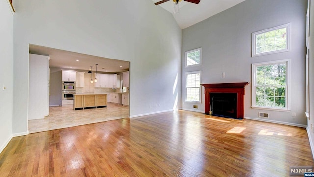 unfurnished living room featuring ceiling fan, a healthy amount of sunlight, a high ceiling, and light wood-type flooring