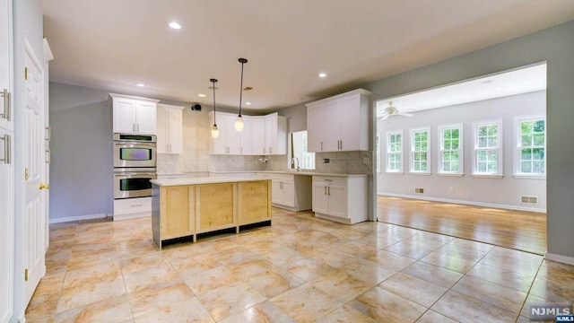 kitchen featuring decorative light fixtures, a kitchen island, white cabinetry, and double oven