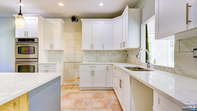 kitchen with sink, hanging light fixtures, stainless steel double oven, light stone counters, and white cabinets