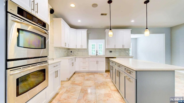 kitchen featuring double oven, tasteful backsplash, decorative light fixtures, a kitchen island, and white cabinetry