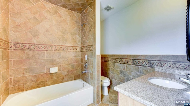 full bathroom featuring sink, tiled shower / bath, tile walls, and toilet