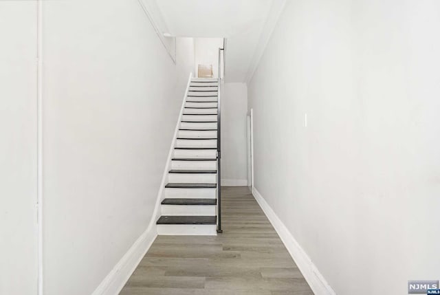 stairs with wood-type flooring and crown molding