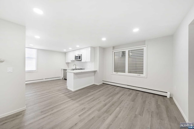 unfurnished living room featuring baseboard heating, light hardwood / wood-style flooring, and sink