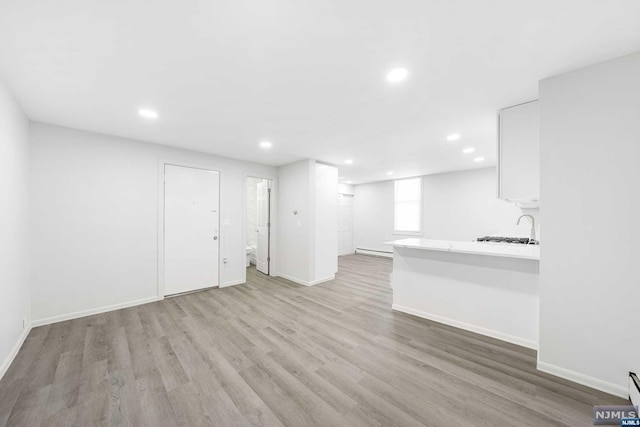 unfurnished living room with light hardwood / wood-style floors, sink, and a baseboard heating unit