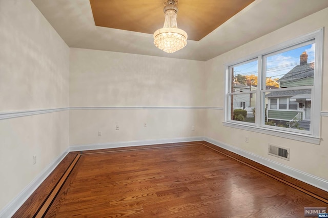 spare room with hardwood / wood-style flooring, a raised ceiling, and a chandelier