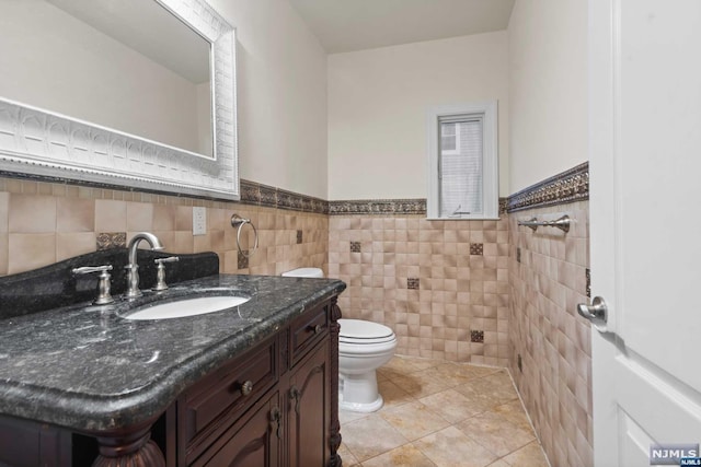 bathroom with tile patterned flooring, vanity, toilet, and tile walls