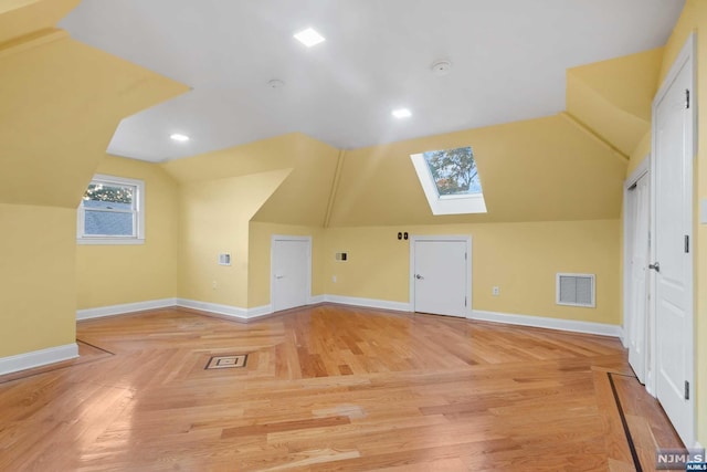 additional living space featuring vaulted ceiling with skylight and hardwood / wood-style flooring