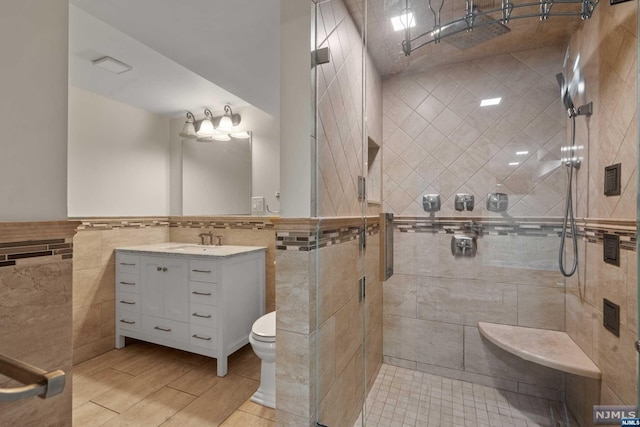 bathroom featuring toilet, vanity, tile walls, and walk in shower