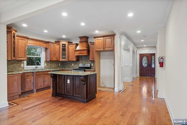 kitchen featuring light wood-type flooring, stainless steel range, a kitchen island, light stone counters, and custom range hood