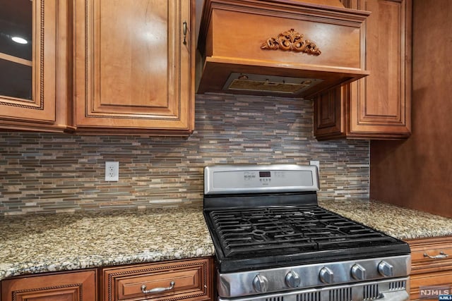 kitchen featuring light stone counters, stainless steel range oven, premium range hood, and tasteful backsplash