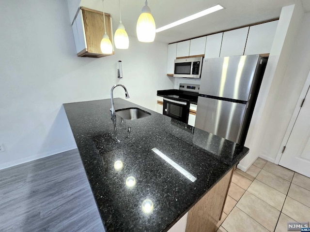 kitchen with pendant lighting, sink, dark stone countertops, appliances with stainless steel finishes, and white cabinetry