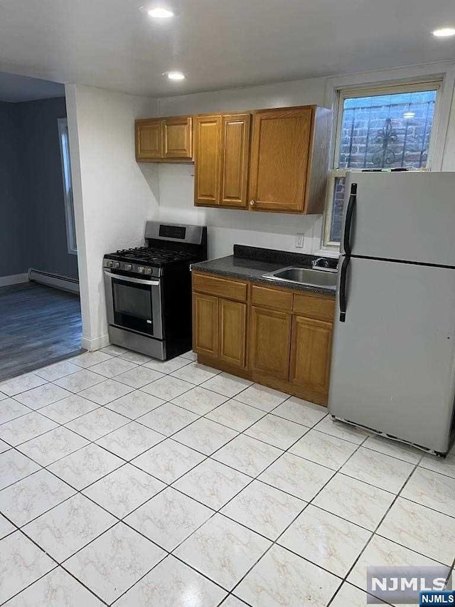 kitchen featuring sink, stainless steel gas range, light hardwood / wood-style floors, a baseboard radiator, and white fridge