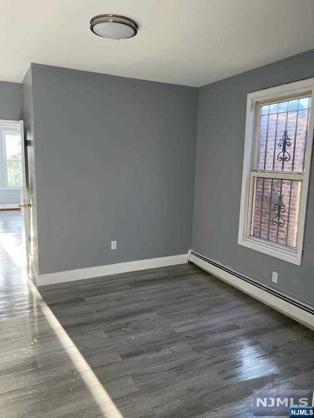 unfurnished room with dark hardwood / wood-style flooring and a baseboard heating unit