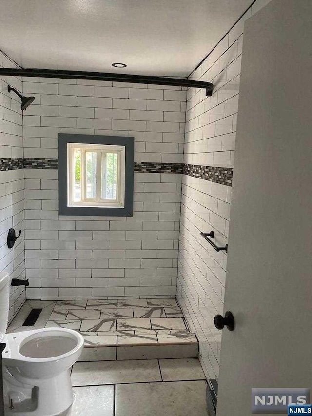 bathroom featuring a tile shower, tile patterned floors, and toilet