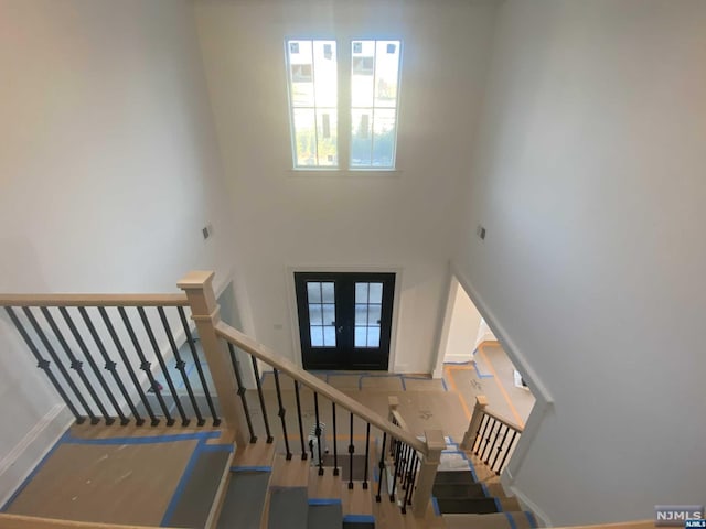 staircase with french doors, a towering ceiling, and wood-type flooring