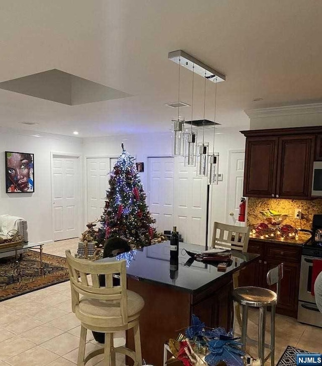 kitchen featuring dark brown cabinetry, range with electric cooktop, backsplash, a kitchen bar, and light tile patterned floors