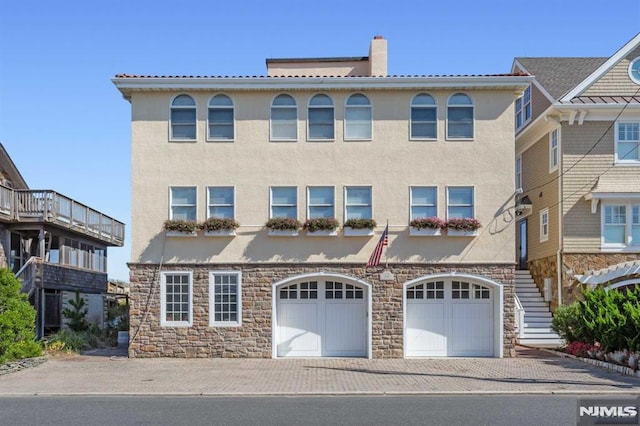 view of front of home featuring stairs, driveway, a chimney, and stucco siding