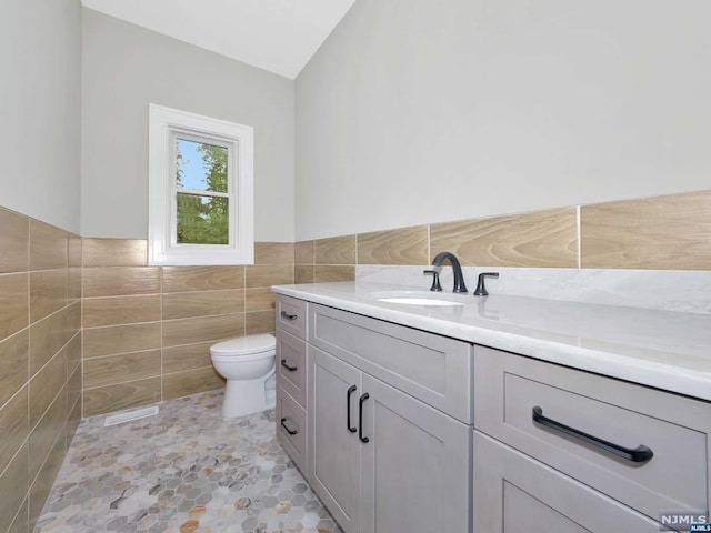 bathroom featuring vanity, tile walls, tile patterned flooring, toilet, and lofted ceiling