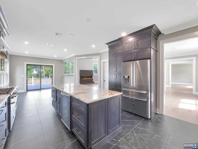 kitchen featuring dark brown cabinetry, a center island, light stone counters, crown molding, and high end appliances