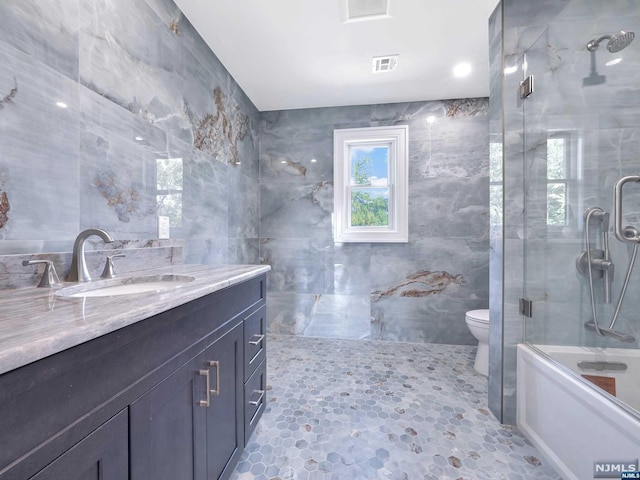 full bathroom with vanity, combined bath / shower with glass door, tile walls, and toilet