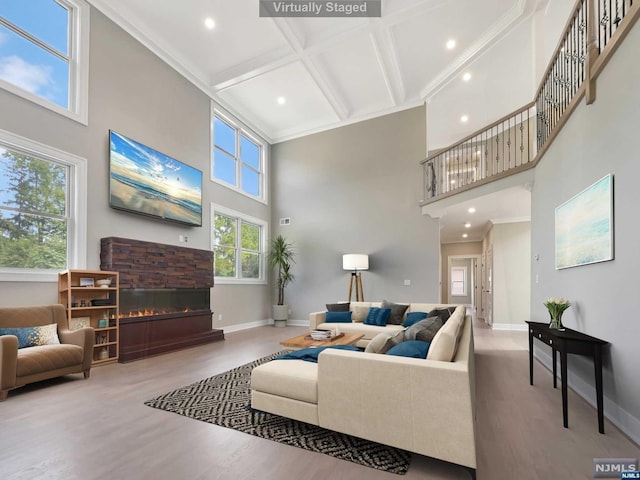 living room featuring hardwood / wood-style floors, a high ceiling, coffered ceiling, a stone fireplace, and ornamental molding