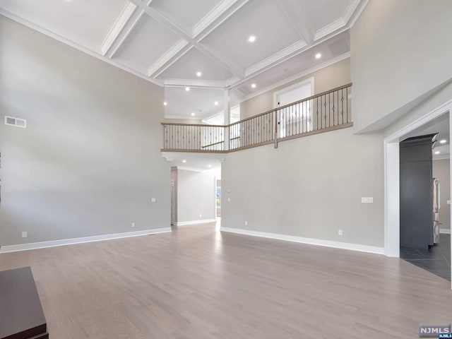 unfurnished living room featuring beam ceiling, a towering ceiling, hardwood / wood-style flooring, and coffered ceiling