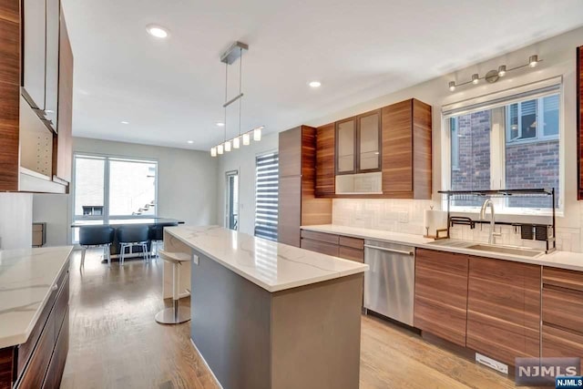 kitchen featuring pendant lighting, dishwasher, a center island, sink, and light hardwood / wood-style floors