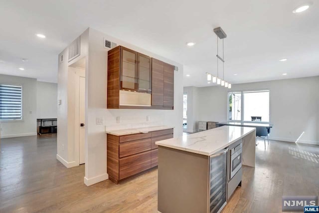 kitchen with beverage cooler, light stone counters, light hardwood / wood-style floors, decorative light fixtures, and a kitchen island