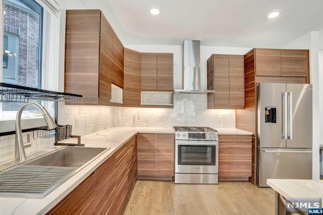 kitchen with sink, light hardwood / wood-style flooring, wall chimney exhaust hood, tasteful backsplash, and stainless steel appliances