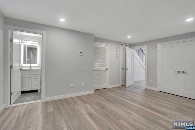 unfurnished bedroom featuring light wood-type flooring, ensuite bath, and sink