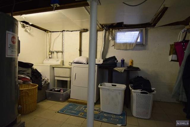 basement featuring water heater, sink, light tile patterned flooring, and washer and dryer