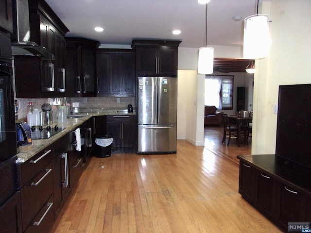 kitchen featuring tasteful backsplash, light wood-style flooring, freestanding refrigerator, black electric stovetop, and wall chimney range hood